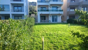 Une cour avec une pelouse bien entretenue, un espace aménagé avec une table et des chaises, et un bâtiment doté de balcons et de fenêtres.