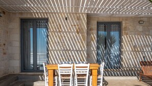 Eine Terrasse im Freien mit Holztisch und weißen Stühlen, einer Steinmauer und einer Pergola.