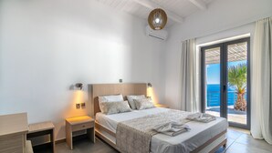 Ein modernes Schlafzimmer mit einem großen Bett, Nachttischen, einem Schreibtisch und Meerblick durch eine Glastür.