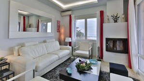 Una sala de estar moderna con un sofá blanco, una mesa de centro con adornos, una chimenea y ventanas grandes con cortinas rojas.