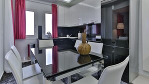 Una cocina moderna con armarios blancos, una mesa de comedor de cristal y cortinas rojas.