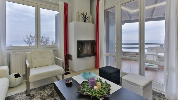Una sala de estar moderna con chimenea, ventanas amplias y vista al mar.