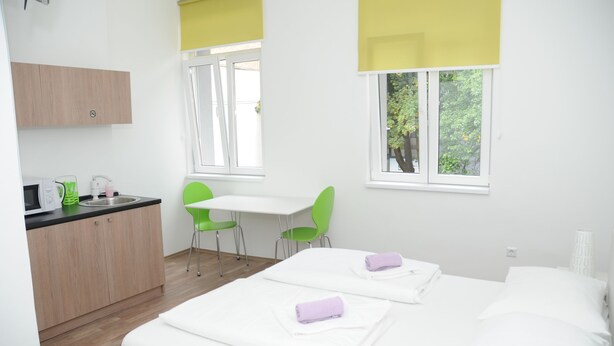 A modern hotel room with a bed, a desk, and a chair. There is a window with a view of trees.