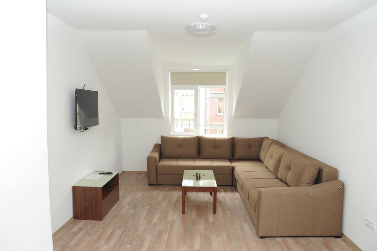 A modern living room with a brown sectional sofa, a small wooden coffee table, and a mounted TV.