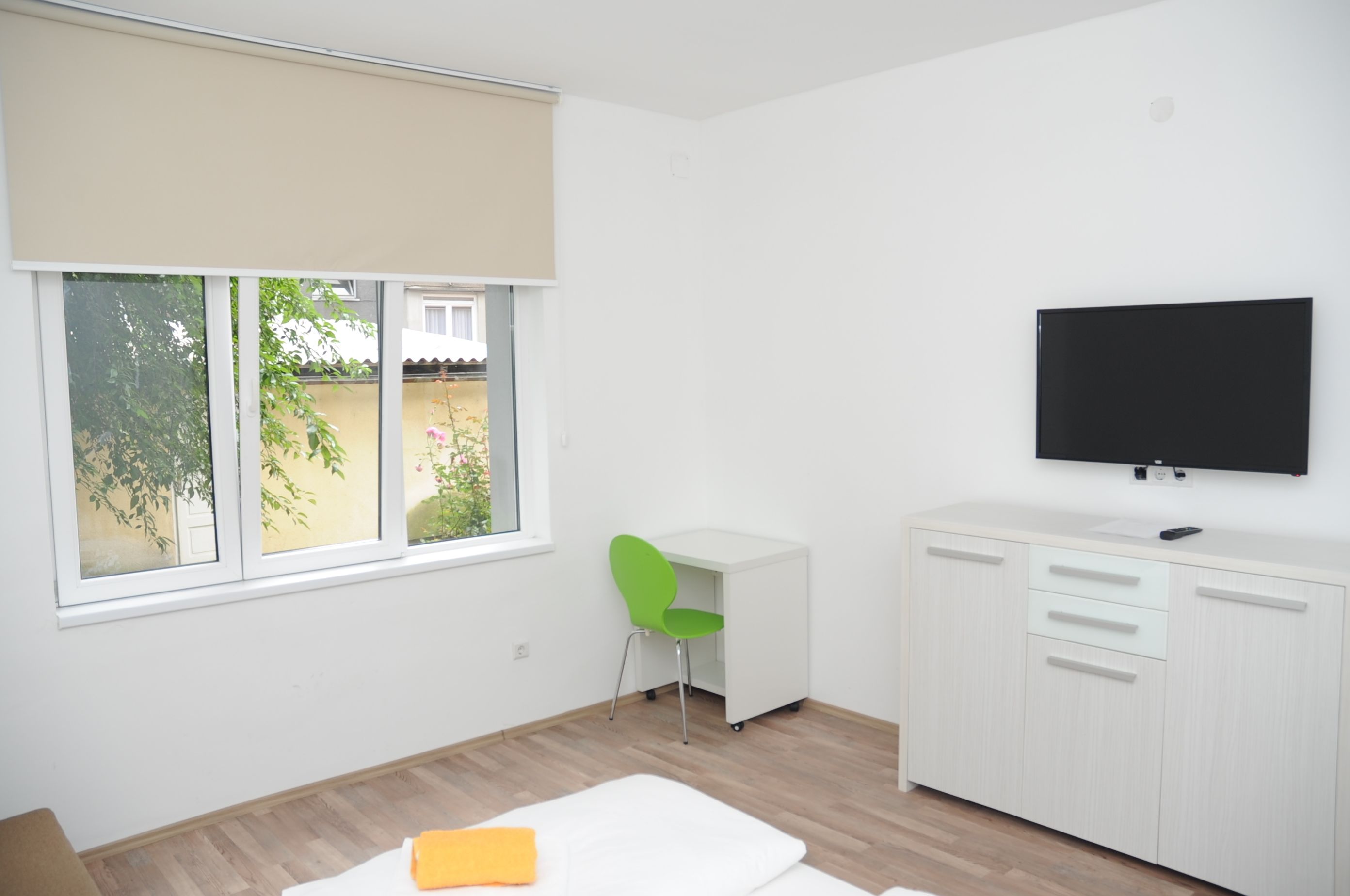 A modern room with a large window, a desk, a chair, and a TV mounted on the wall.