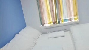 A single bed with white bedding, a nightstand with a lamp, and a window with striped curtains. - Leman House (London)