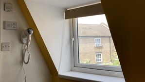 A room with a slanted ceiling, a window with a white frame, a radiator, and a hairdryer plugged in. - Leman House (London)