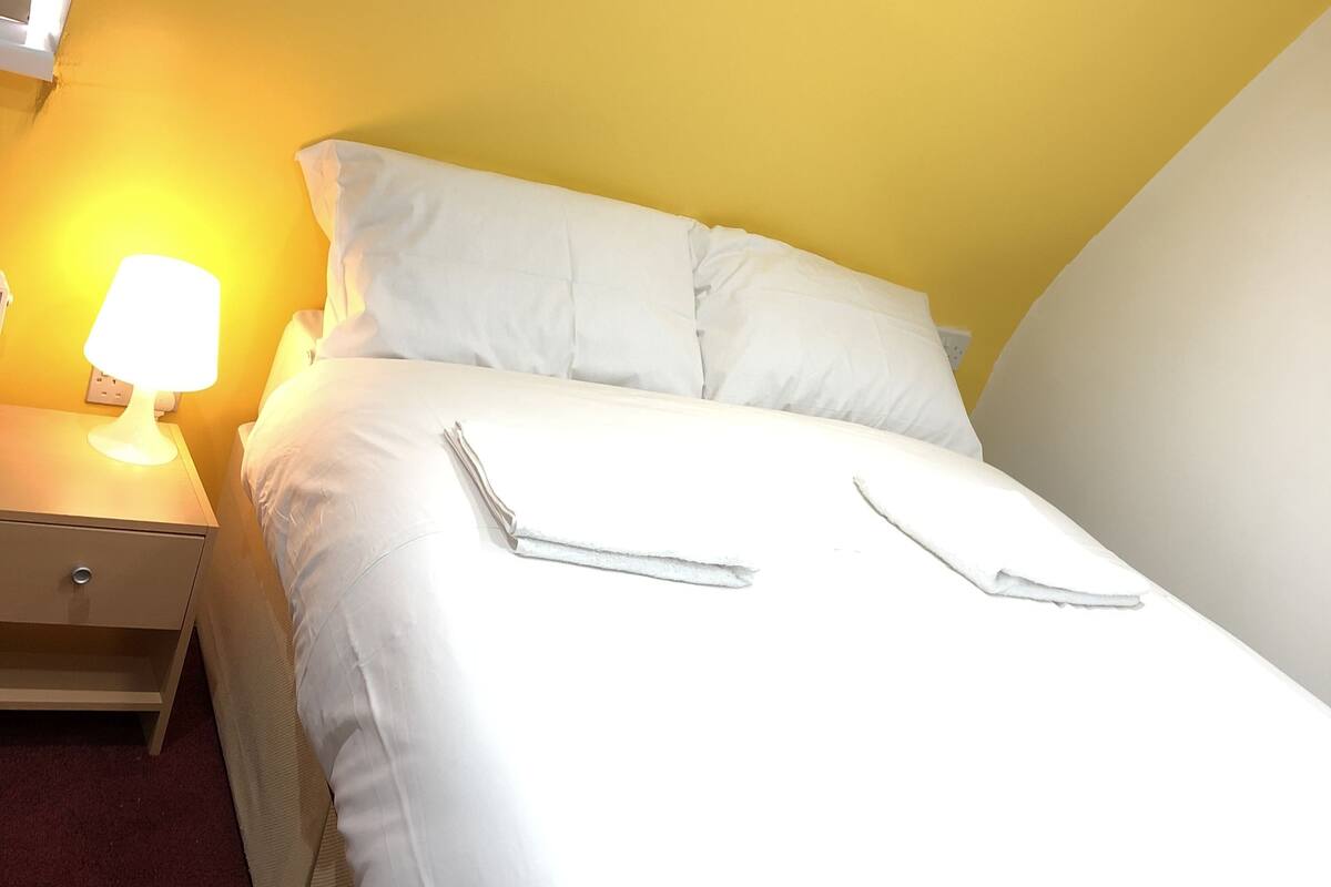 A neatly made bed with white linens in a room with yellow walls.