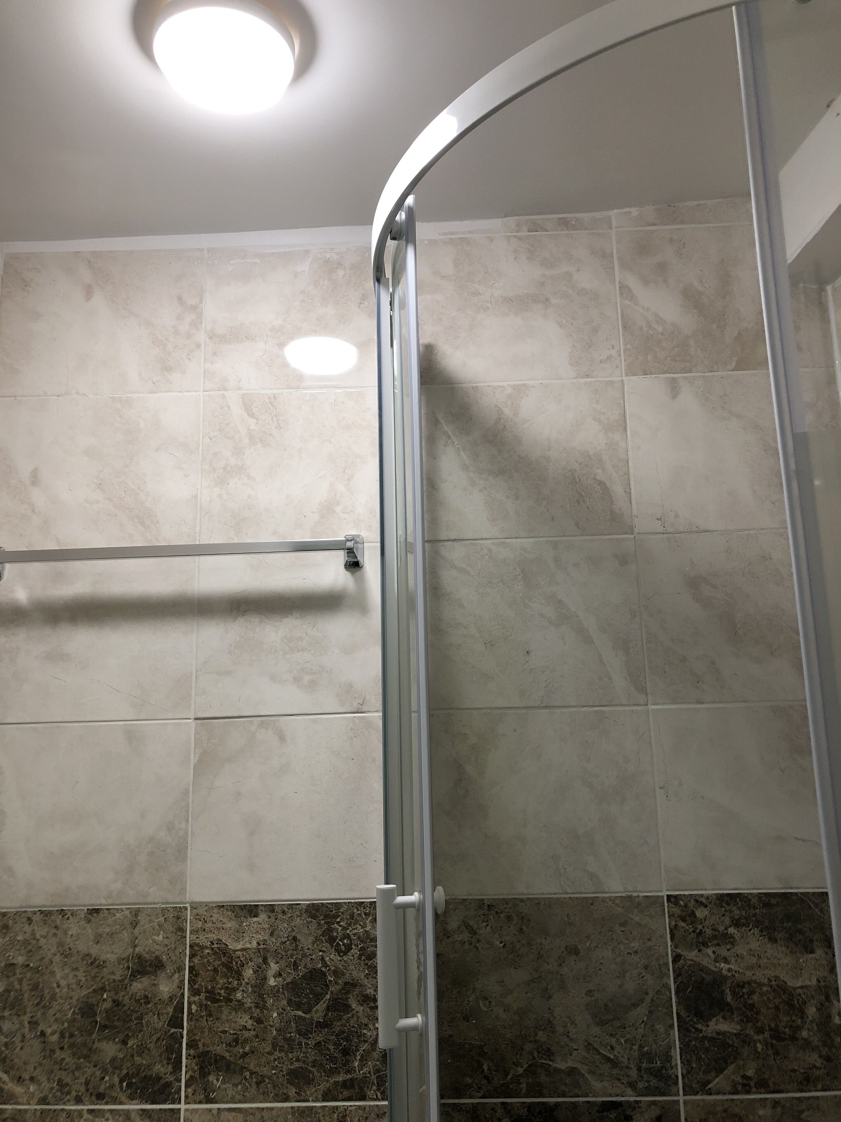 A shower area with a glass door, a towel rack, and a ceiling light.