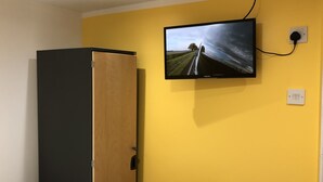 A room with a yellow wall, a mounted television displaying a landscape, and a wooden wardrobe. - Leman House (London)