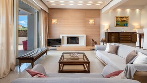 A modern living room with a fireplace, sofa, and television. - Vasiliki Villa with Private Pool (Ιαλυσός)