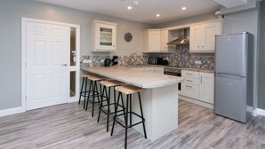 A modern kitchen with a large island, bar stools, white cabinets, and a stainless steel refrigerator. - University Road Apartments (Belfast)