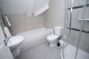 A modern bathroom with a bathtub, toilet, and glass-enclosed shower. - University Road Apartments (Belfast)