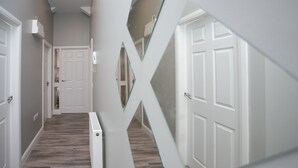 A hallway with white doors, a wooden floor, and a white wall with a geometric design. - University Road Apartments (Belfast)