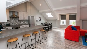 A modern kitchen with a central island, bar stools, and a dining area with a red sofa. - University Road Apartments (Belfast)