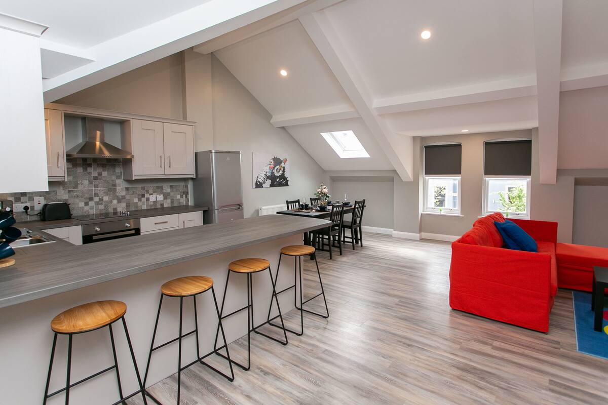 A modern kitchen with a central island, bar stools, and a dining area with a red sofa.