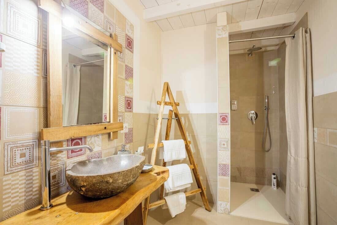 Un bagno con un lavandino in pietra, una scala in legno e una doccia a filo pavimento.