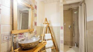 Un bagno con un lavandino in pietra, una scala in legno e una doccia a filo pavimento.