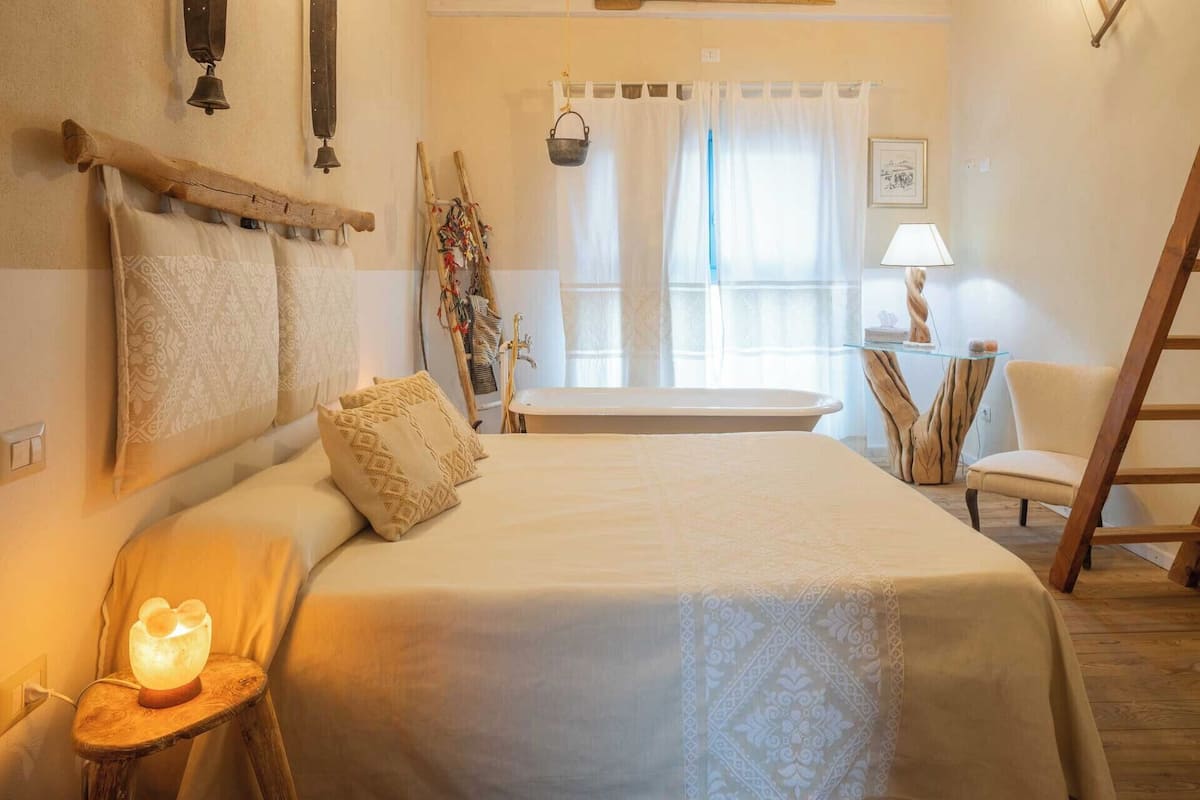 Ein gemütliches Schlafzimmer mit einem Bett, einem Nachttisch mit einer Salzlampen, einem Sessel, einem kleinen Tisch mit einer Lampe und einer Leiter.