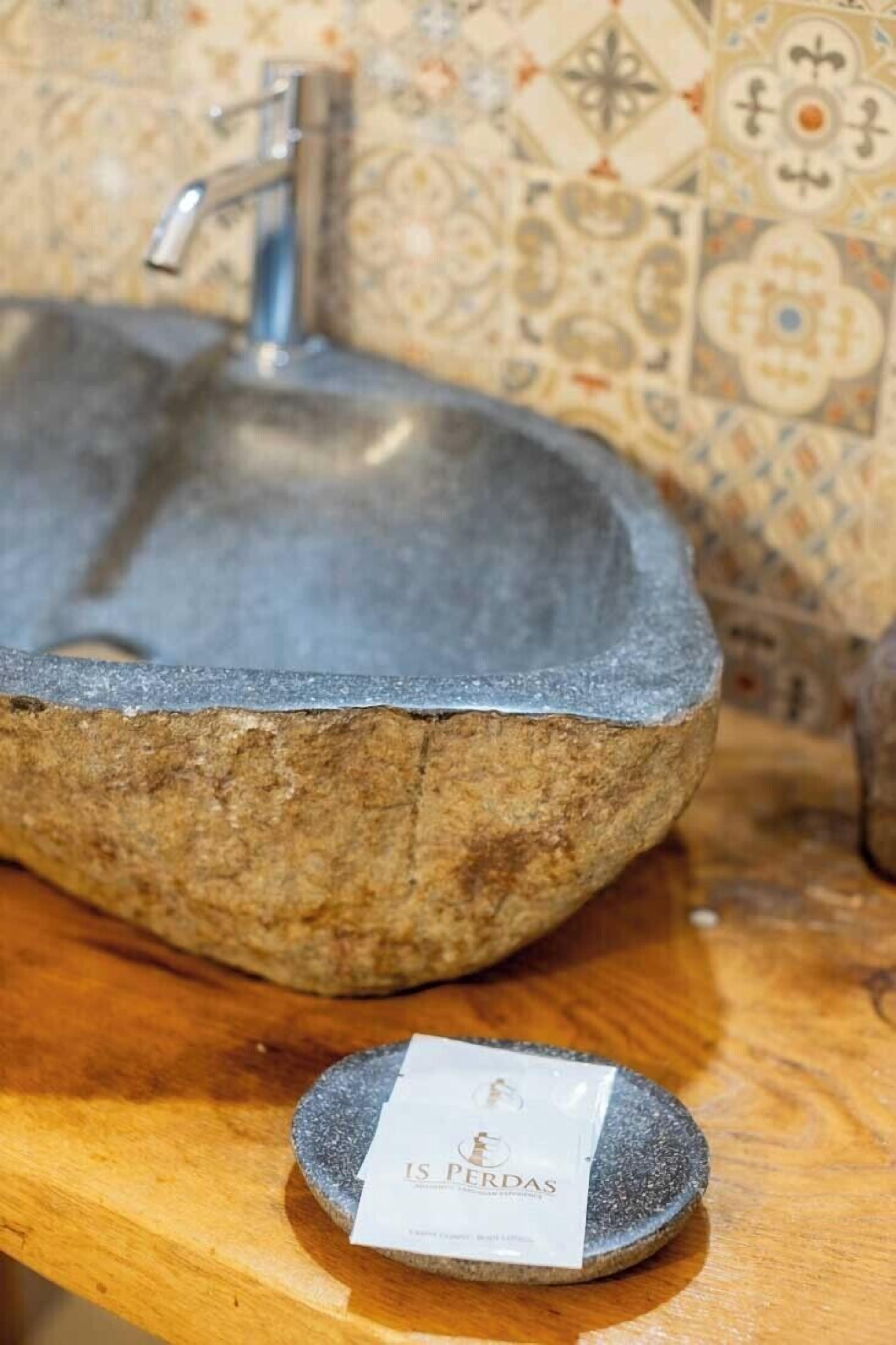 Ein Steinwaschbecken mit einem Wasserhahn in einem Badezimmer mit gefliestem Rücksprühfeld.