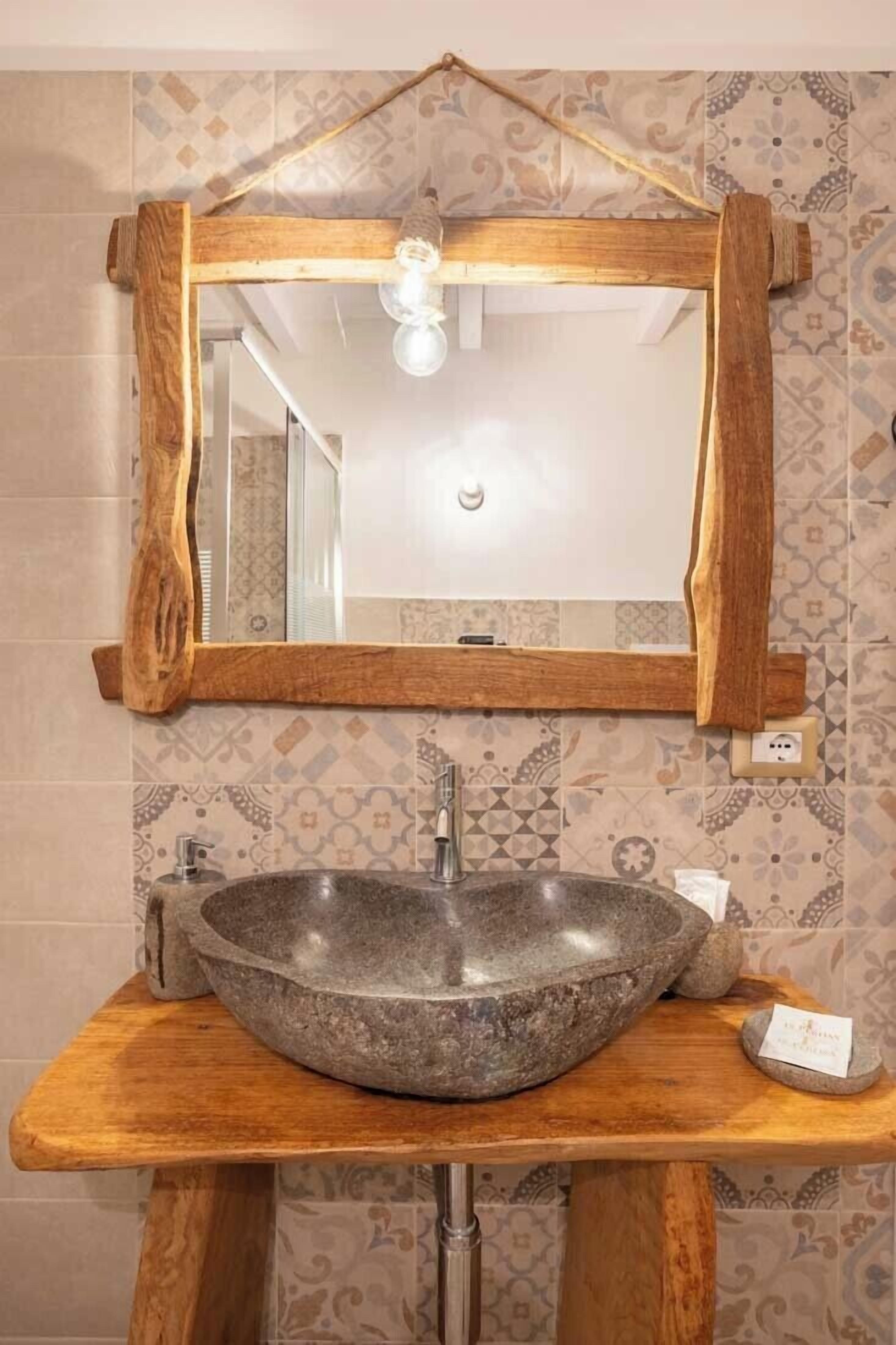 A bathroom with a wooden vanity, a stone sink, and a mirror with a wooden frame.