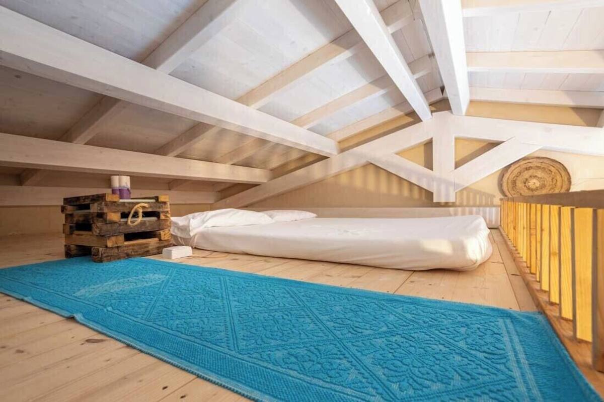 Ein Schlafzimmer im Dachgeschoss mit hohen Decken, Holzboden, einem blauen Teppich mit Muster, einem Bett und einer kleinen Holzkiste.