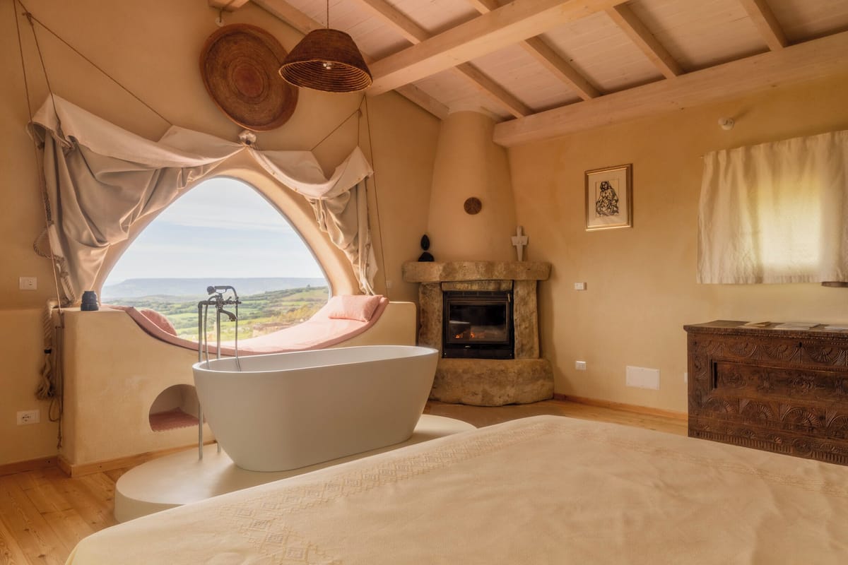 Ein Schlafzimmer mit großem Fenster, Badewanne, Kamin und Holzboden.