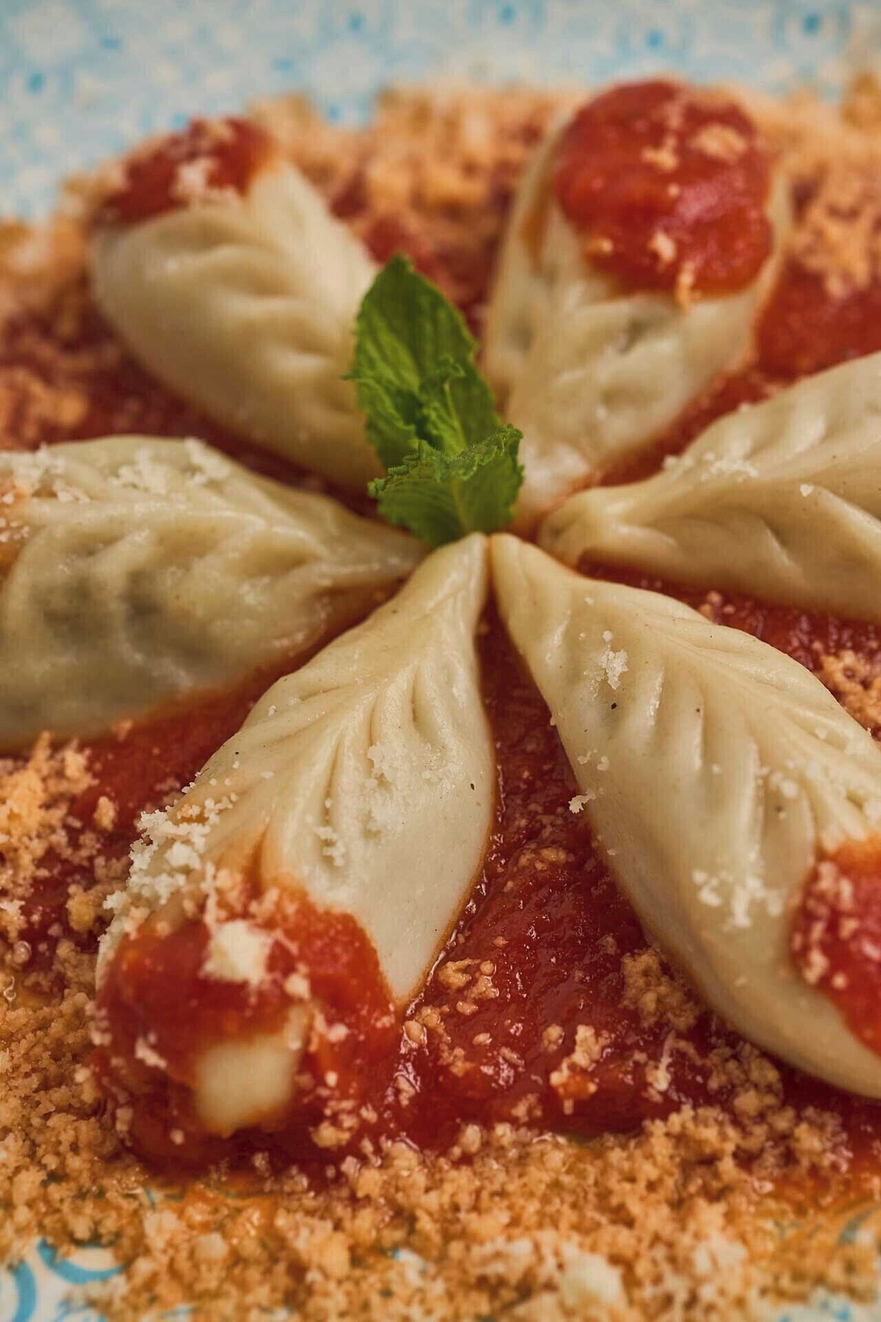 A plate of ravioli with a tomato-based sauce and grated cheese, garnished with a mint leaf.