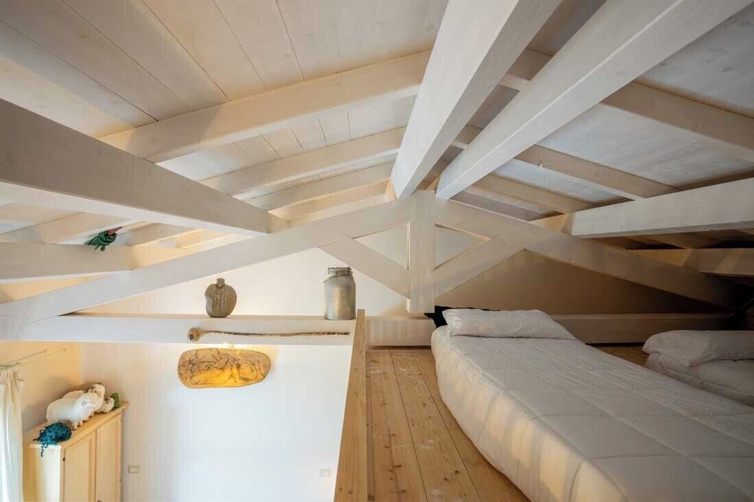 An attic bedroom with exposed wooden beams, a bed, a small table, and a decorative wall piece.