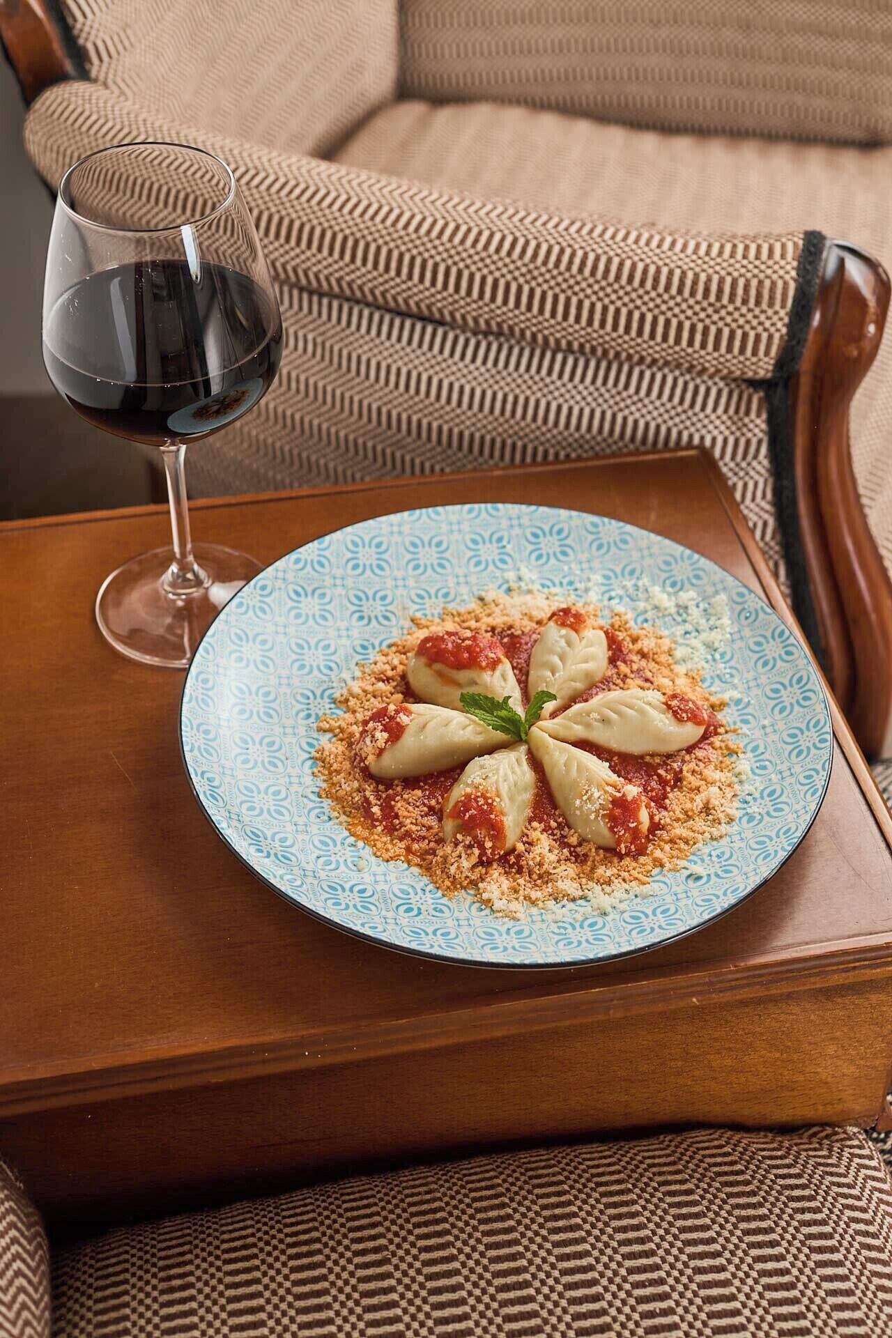 Een bord met gevulde dumplings, een garnering, een glas rode wijn en een gestreept kussen op een houten tafel.