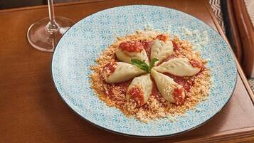 Een bord met gevulde dumplings, een garnering, een glas rode wijn en een gestreept kussen op een houten tafel.
