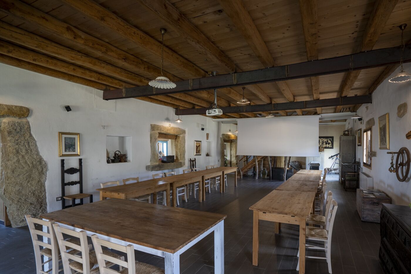 A rustic dining hall with long wooden tables and benches, stone walls, and exposed wooden beams.