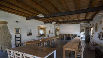 A rustic dining hall with long wooden tables and benches, stone walls, and exposed wooden beams.