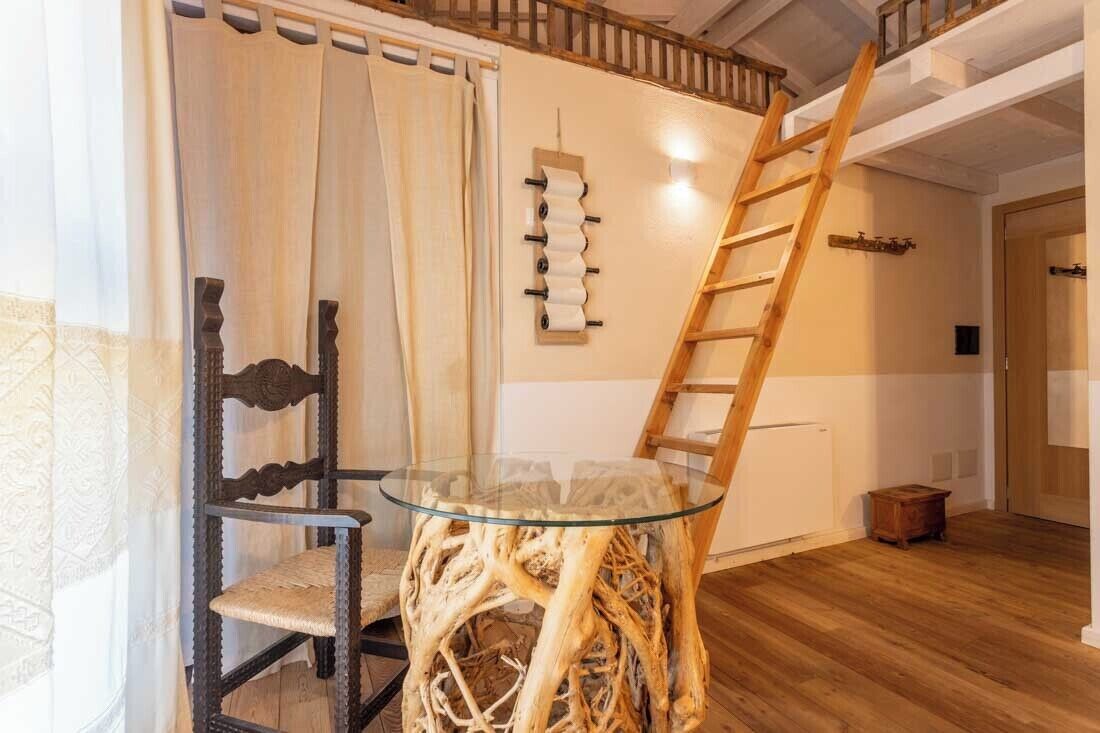 Une pièce avec une table à plateau en verre, entourée d’une chaise, d’une échelle en bois et d’un porte-bobines fixé au mur.