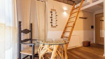Une pièce avec une table à plateau en verre, entourée d’une chaise, d’une échelle en bois et d’un porte-bobines fixé au mur.