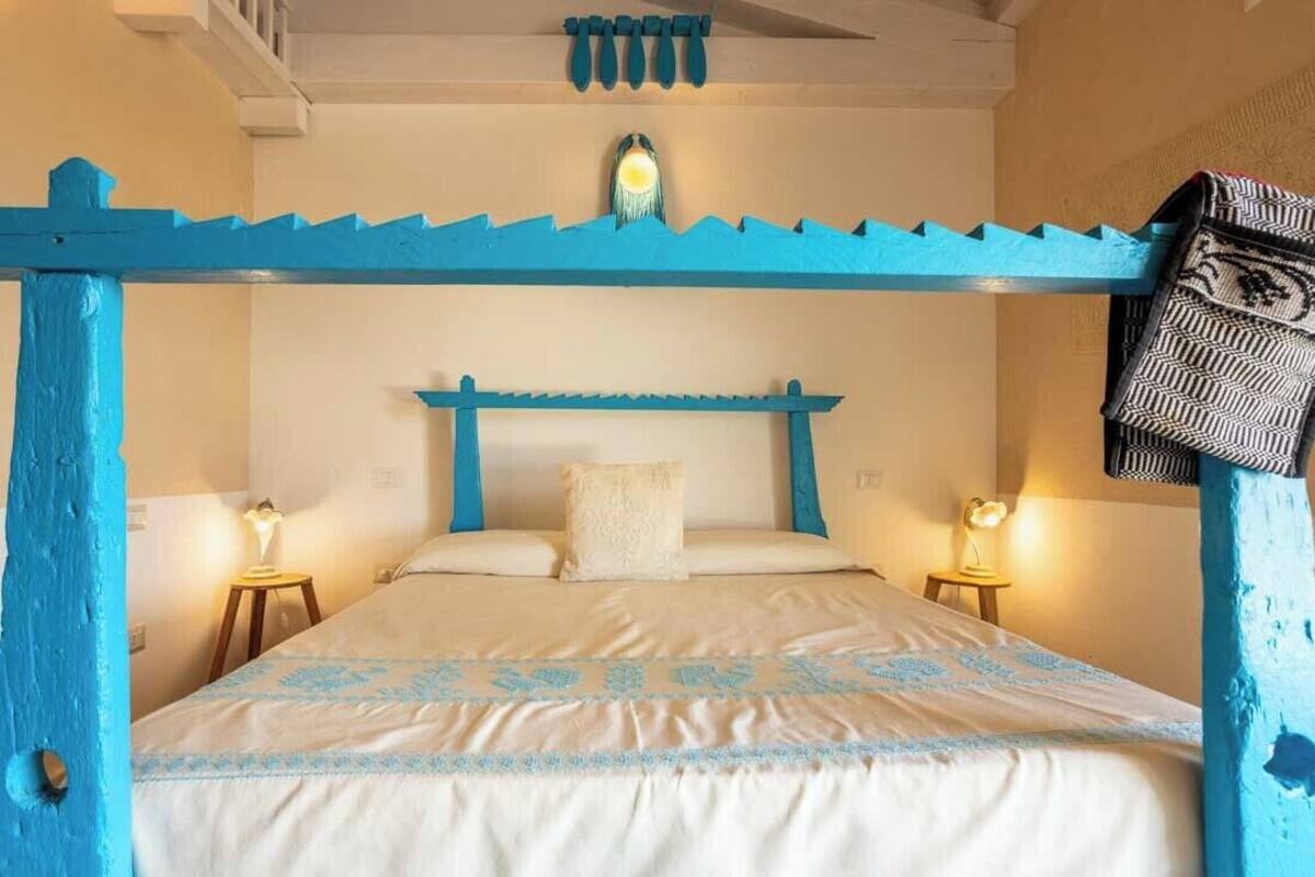 Ein Zimmer mit einem Bett unter einem blauen Baldachin, zwei Nachttische mit Lampen und einer gemusterten Bettdecke.