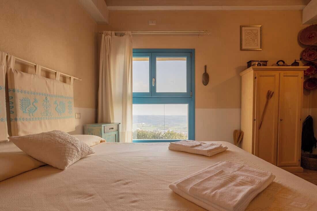 Een slaapkamer met een bed, een raam met gordijnen, een houten garderobe en uitzicht op het landschap.