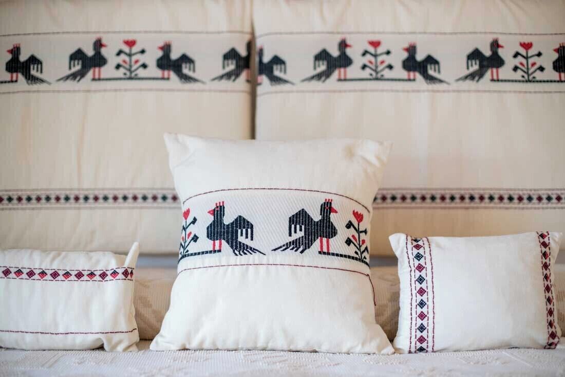 A bed with white bedding and decorative pillows featuring embroidered designs.