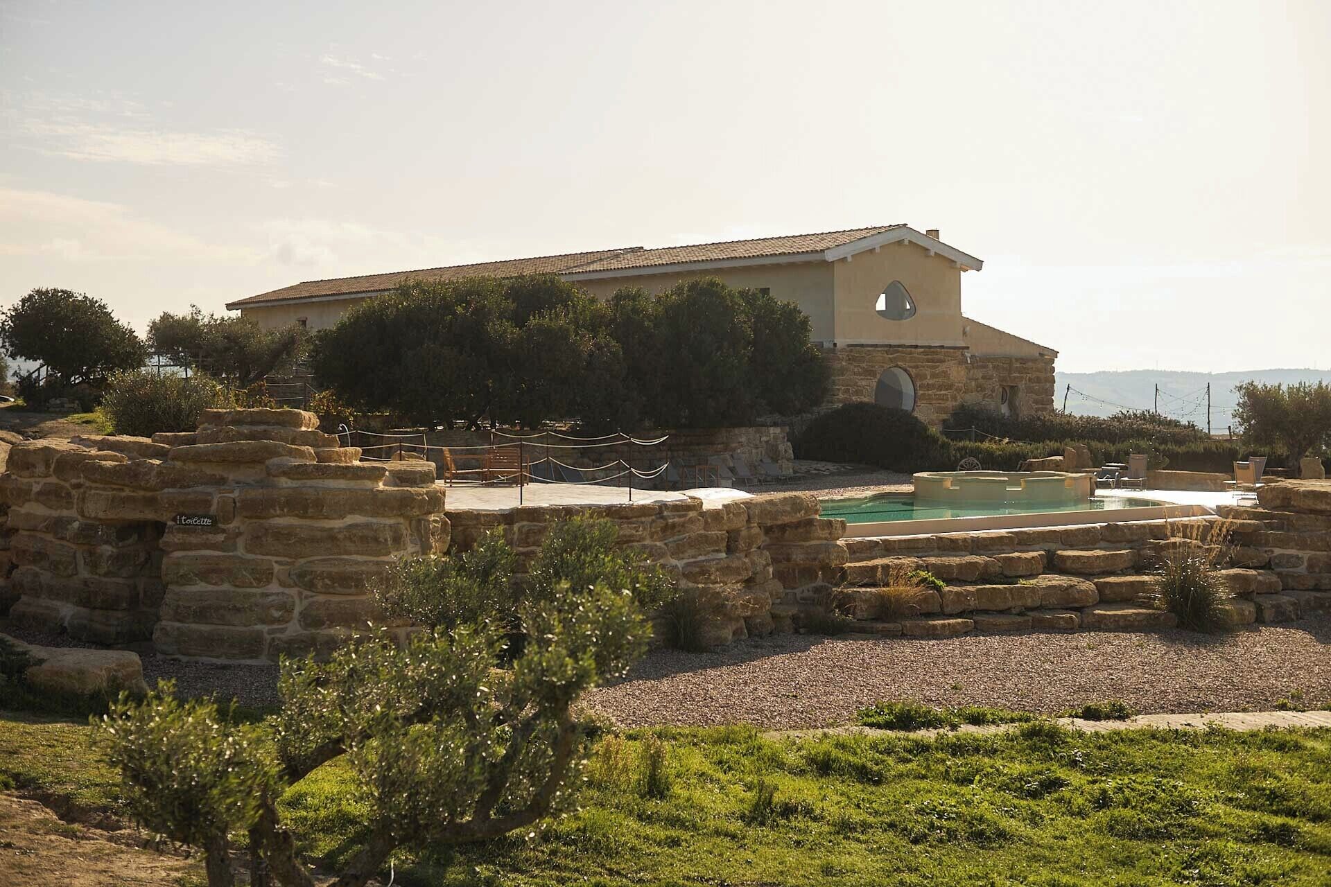 A stone building with a pool, surrounded by greenery and stone walls.