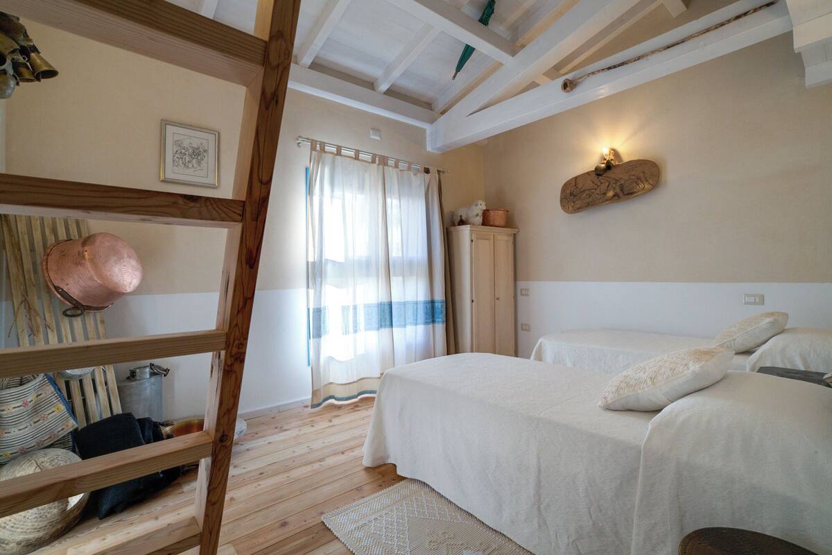 Ein Schlafzimmer mit einer Holzleiter, einem Bett mit weißer Bettwäsche, einem Holzschrank und einer an der Wand befestigten Leuchte.
