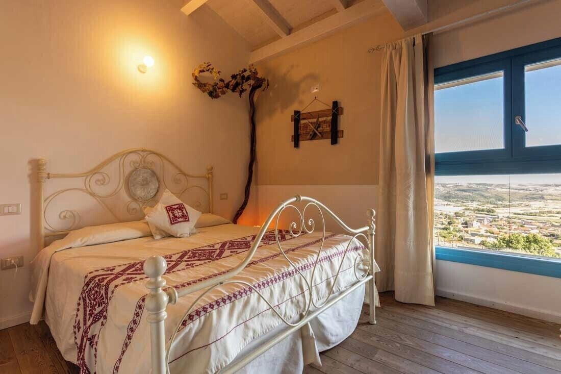 Een slaapkamer met een bed, een wandlamp, uitzicht door een raam en een houten vloer.
