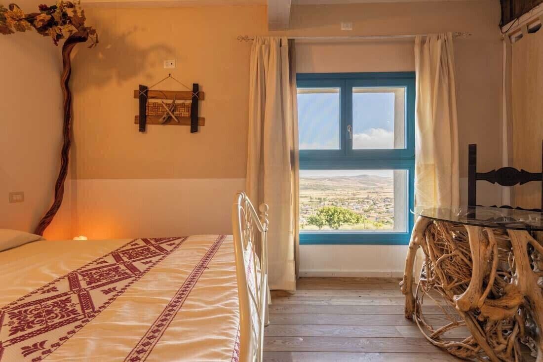 Une chambre à coucher avec un lit, une table en bois, une fenêtre donnant sur un paysage agréable et un élément décoratif en bois fixé au mur.