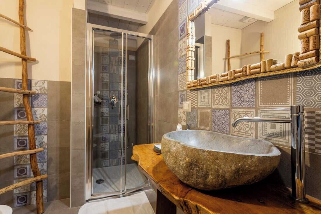 A bathroom with a stone sink, a glass shower enclosure, and patterned tiles.