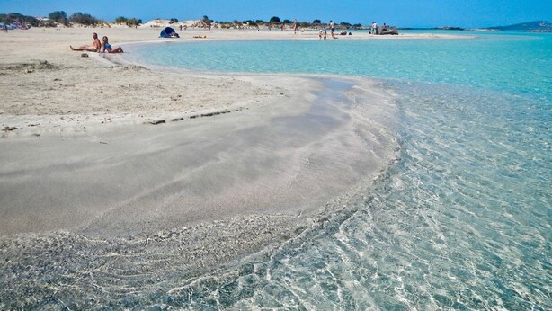 Une plage à l’eau claire où les gens se prélassent sur le sable.
