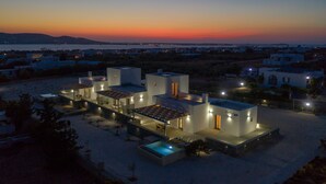 A modern villa with a pool, outdoor seating, and a view of the sea at sunset. - BLUEBELL VILLA SUNRISE (ΚΑΜΠΟΣ)