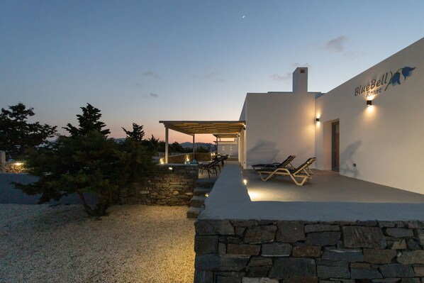A modern outdoor area with a covered seating area, stone walls, and a poolside lounge.