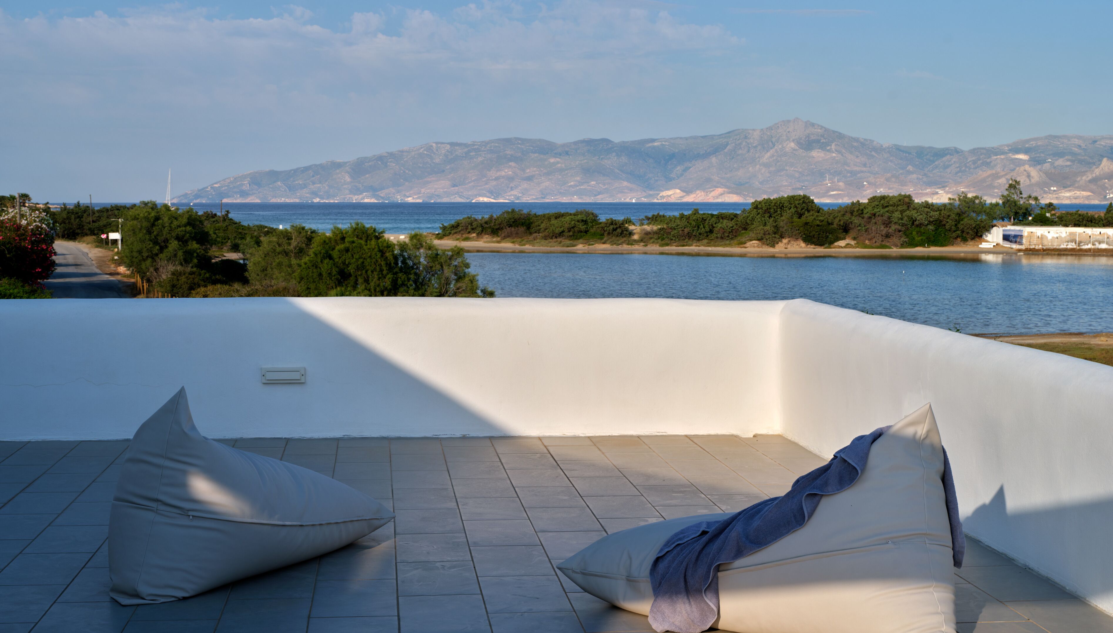 A terrace with a view of the sea and mountains, featuring a white wall and tiled floor.