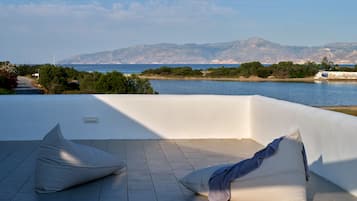 A terrace with a view of the sea and mountains, featuring a white wall and tiled floor.