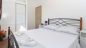 A neatly made bed with white linens and towels, a wooden headboard, a small bedside table with a lamp, and a white nightstand. - Apartments Bruno (Okrug)