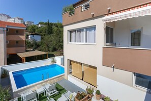 A modern two-story building with a swimming pool, outdoor seating, and a view of surrounding buildings. - Apartments Bruno (Okrug)